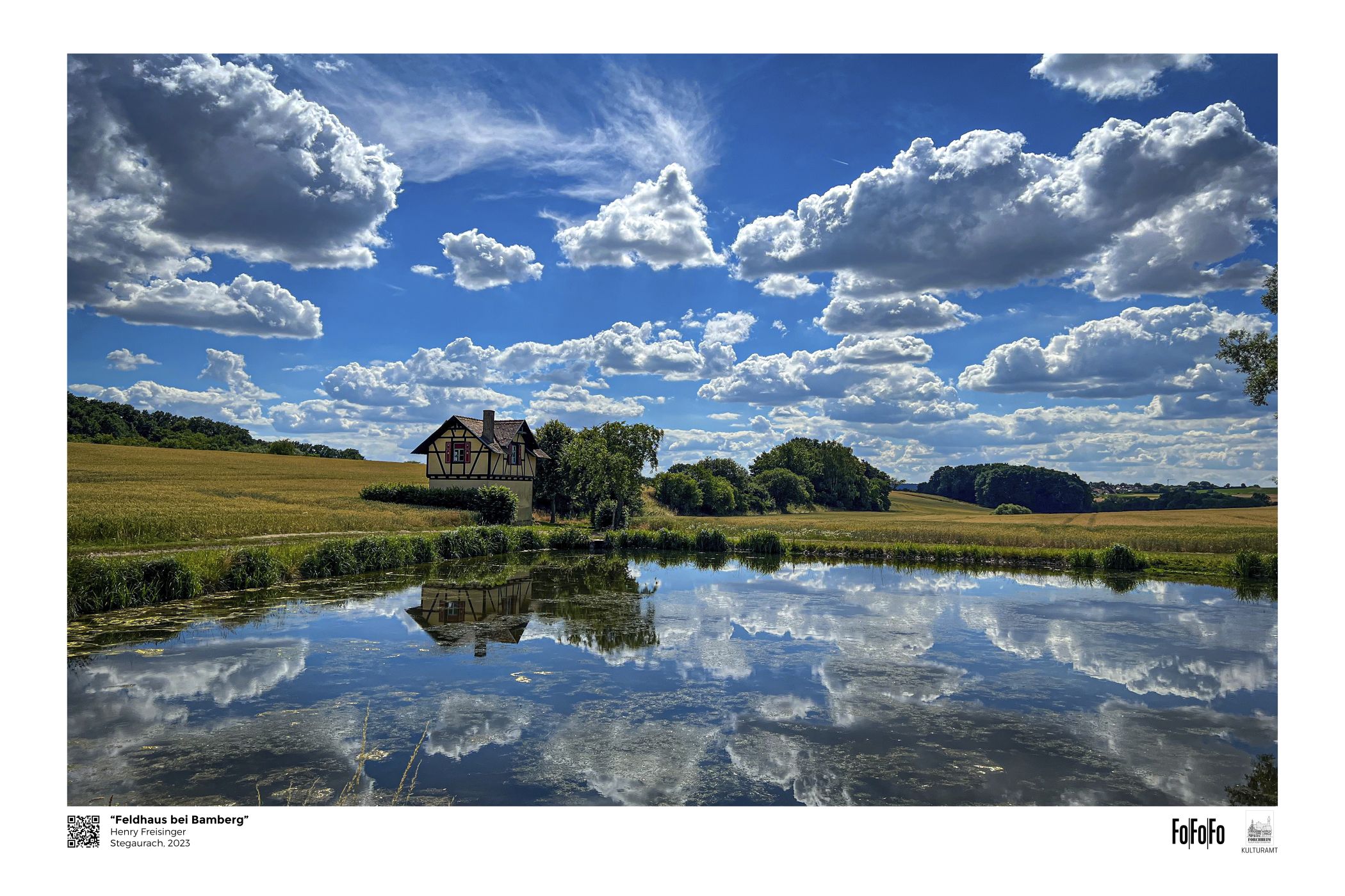 Fachwerkhaus bei Bamberg spiegelt sich im Weiher unter sommerlichem Wolkenhimmel