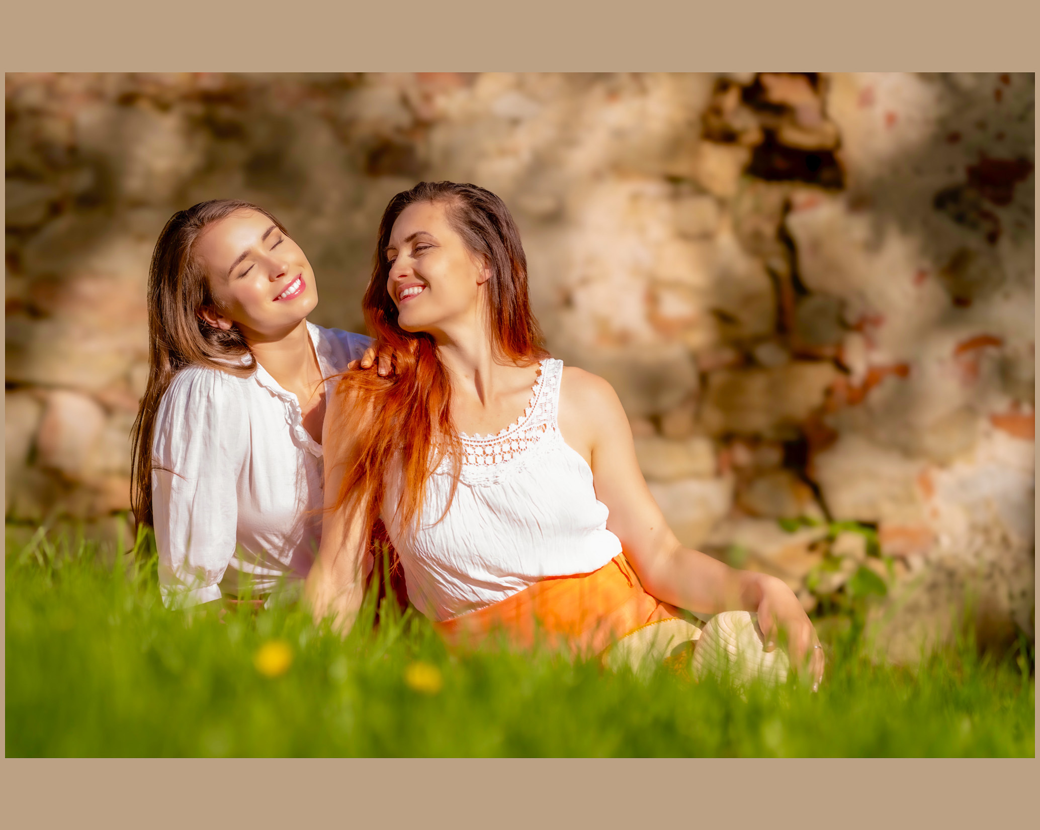 Zwei Frauen sitzen lachend im Gras und genießen die Sonne