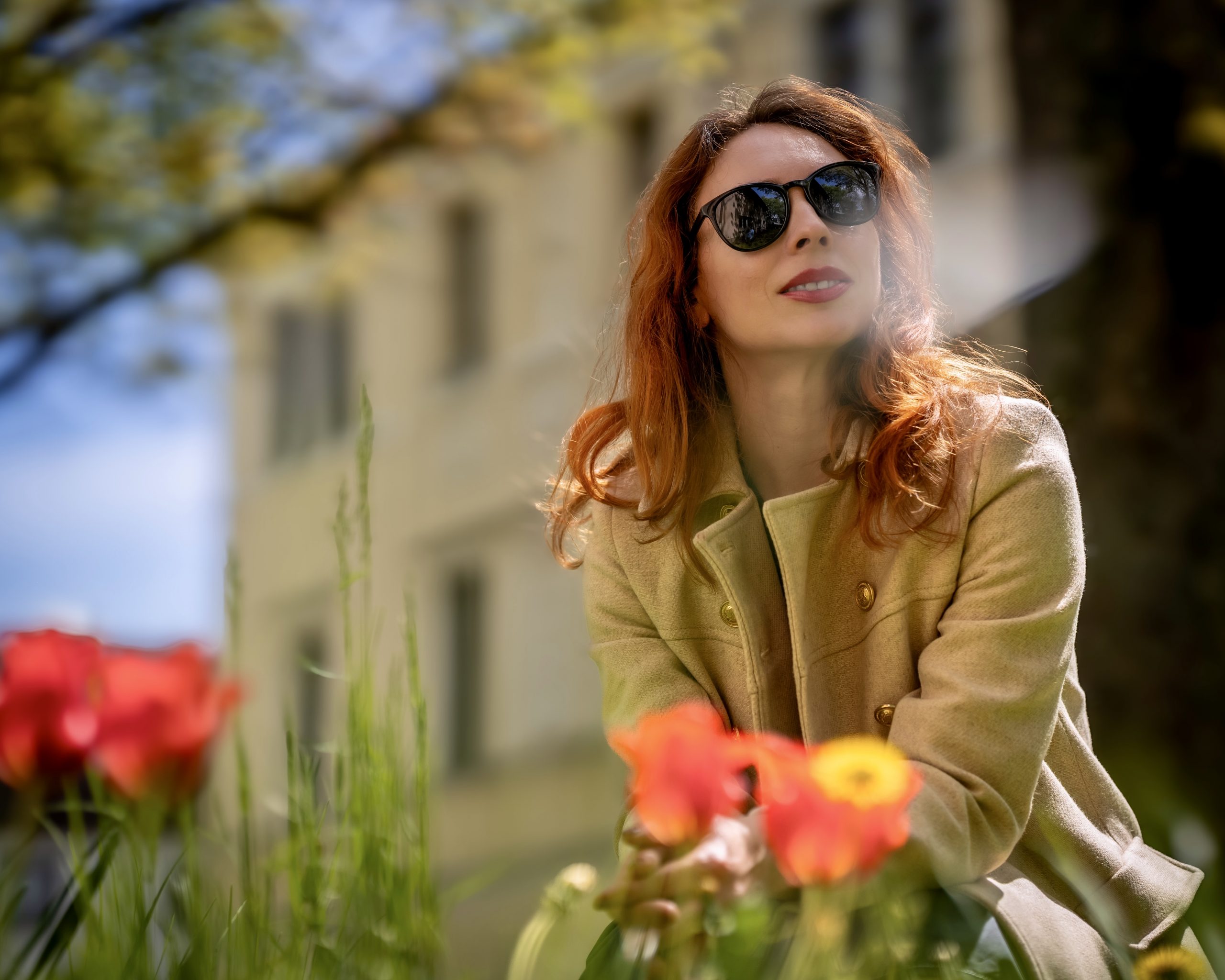 Frau mit Sonnenbrille und rotem Haar im Frühlingsgarten zwischen Blumen