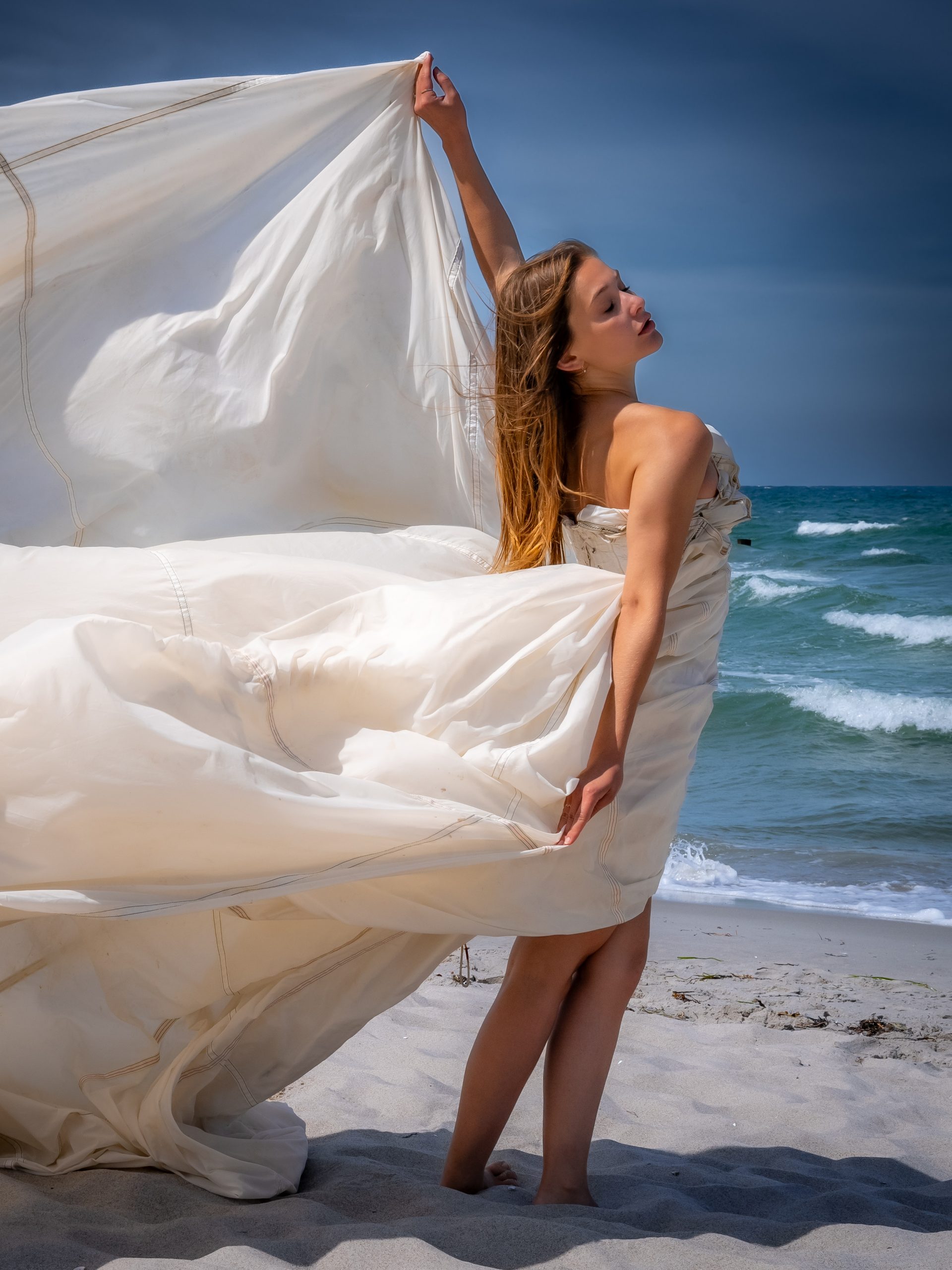 Model am Strand mit wehendem Fallschirm im Wind, elegante Pose