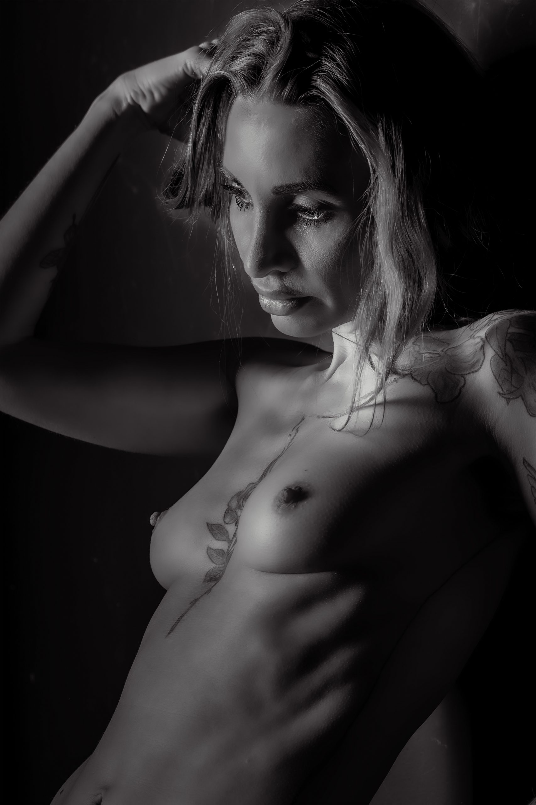 Schwarz-Weiß Aktfoto einer tätowierten Frau mit nachdenklichem Blick