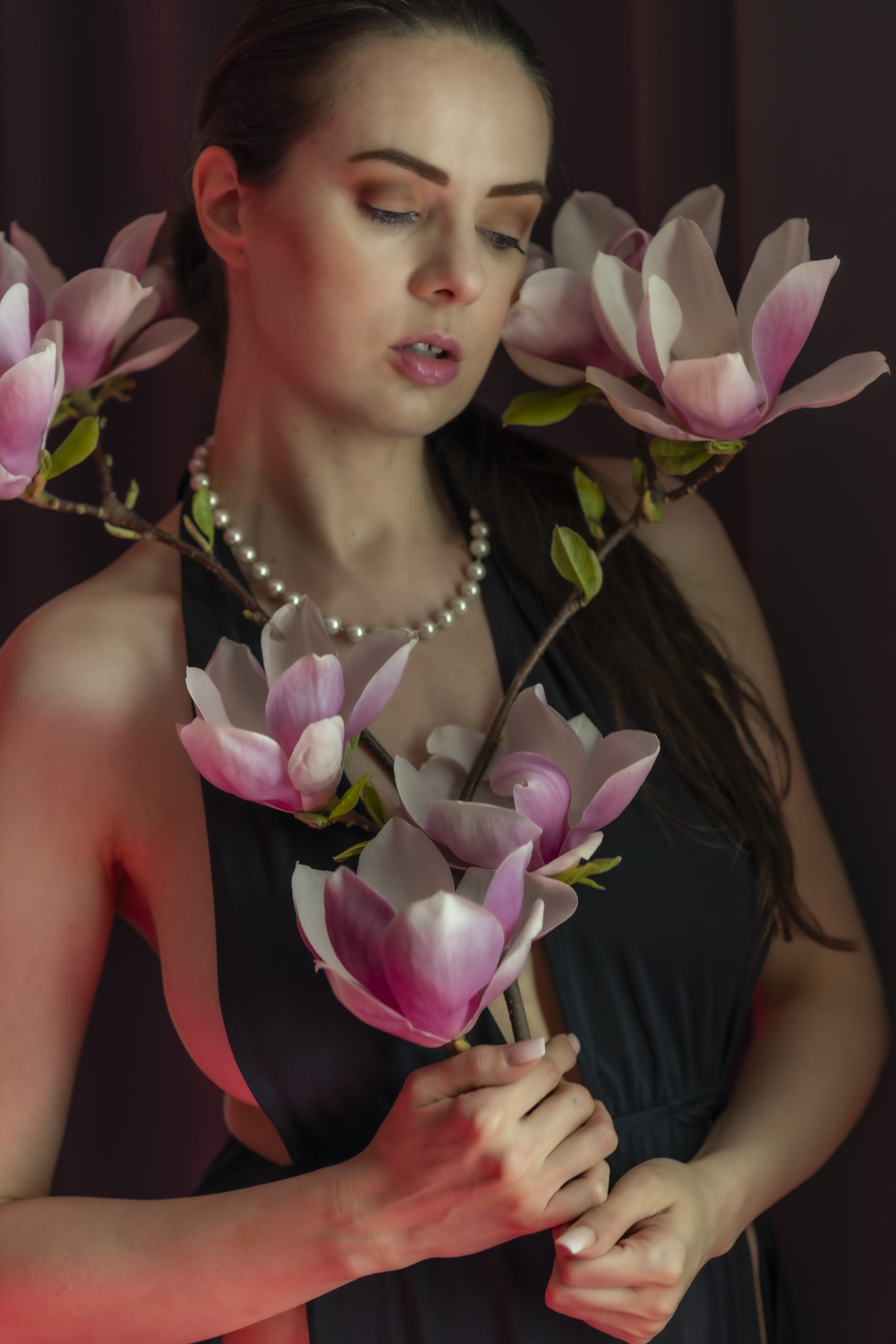 Frau in schwarzem Kleid mit Magnolienzweig und Perlenkette