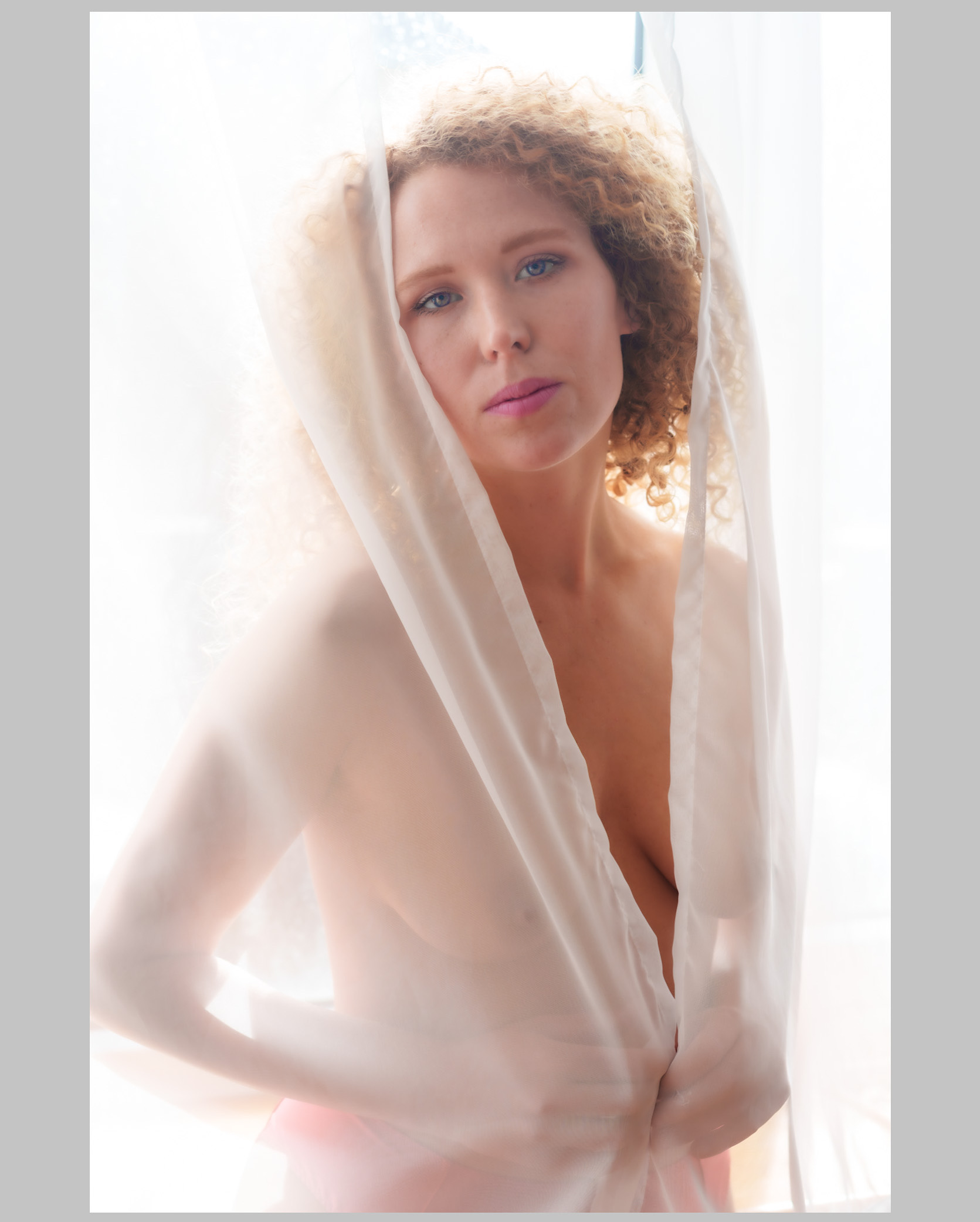 Dieses Bild wirkt wie ein flüchtiger Moment zwischen Traum und Wirklichkeit. Das weiche, überstrahlte Licht legt sich wie ein Schleier über die Szene und lässt die Konturen fast schweben. Der Stoff vor der Person schafft eine natürliche Distanz, die dennoch Nähe ausdrückt — als würde man einen stillen, intimen Gedanken einfangen, nicht den Körper selbst. Der Blick ist sanft, offen und ruhig, getragen von der hellen, fast ätherischen Atmosphäre. So entsteht ein Bild, das weniger zeigt, als es fühlen lässt: eine zarte Berührung aus Licht, Ruhe und leiser Melancholie.