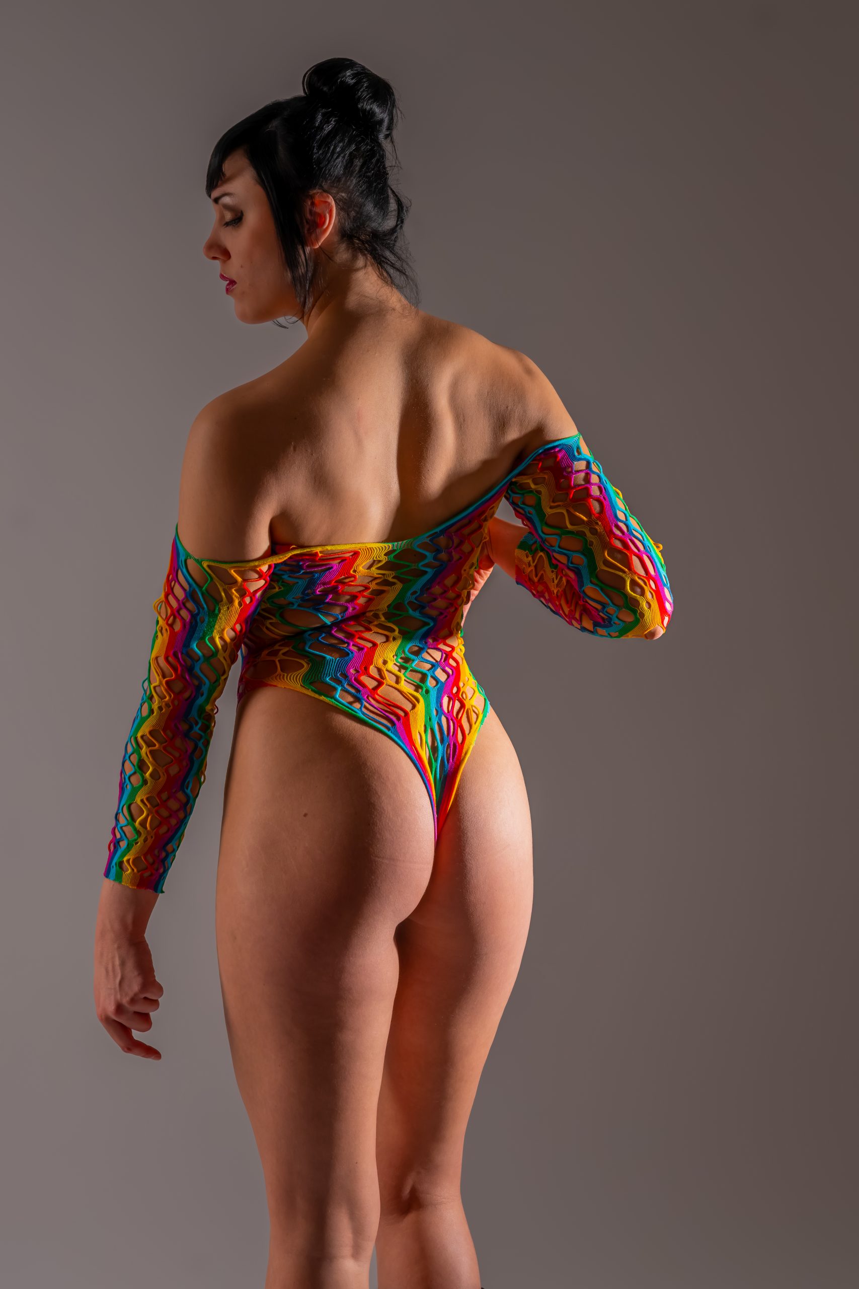 Model Hanna in einem farbintensiven Fashion-Outfit im Studio, von hinten und seitlich fotografiert, mit ruhiger, ausdrucksstarker Pose vor neutralem Hintergrund.