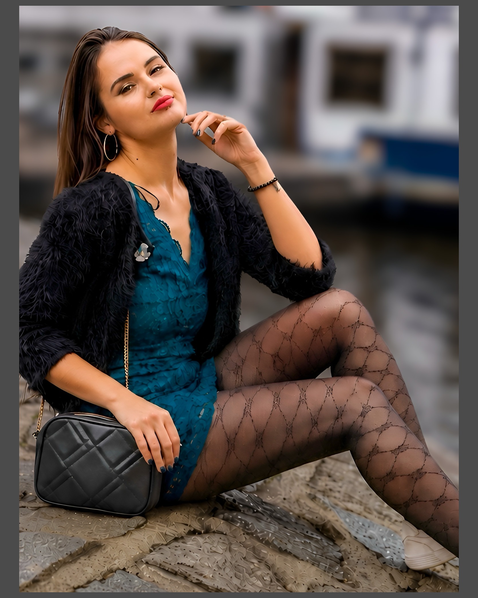 Fashion-Porträt einer jungen Frau im petrolfarbenen Kleid mit grafisch gemusterter transparenter Feinstrumpfhose. Sitzende Pose am Wasser mit schwarzer Handtasche und natürlichem Hintergrund. Fashion- und Legwear-Fotografie von Henry Freisinger.